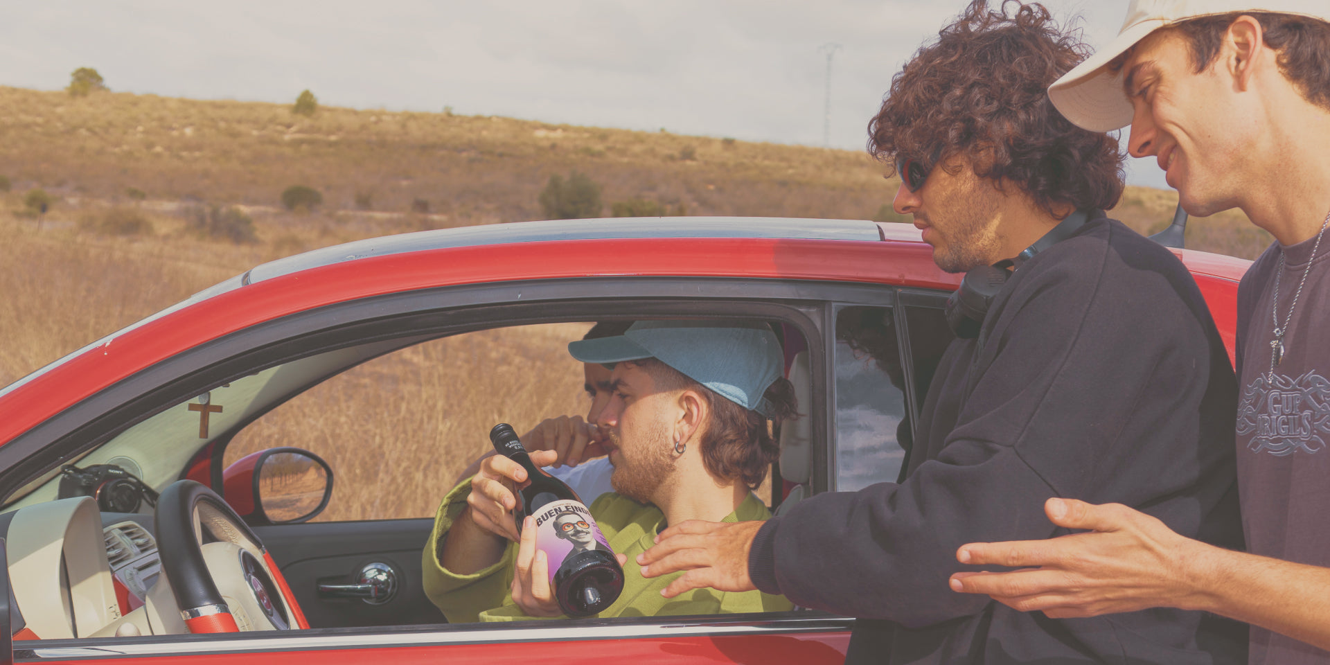 Amigos reunidos alrededor de un coche compartiendo una botella de Buen Finde en un viaje por carretera 