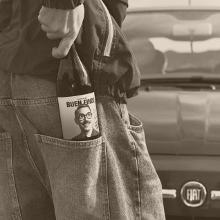 Botella de Buen Finde en el bolsillo trasero de unos vaqueros junto a un coche Fiat, capturando un estilo de vida urbano y relajado