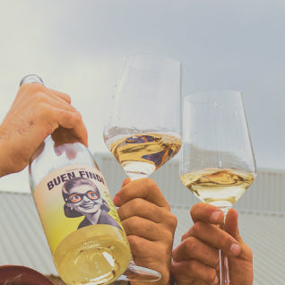 Primer plano de manos brindando con botellas y copas de Buen Finde, celebrando la amistad y los buenos momentos