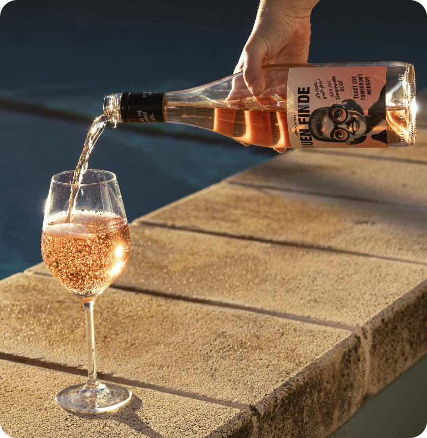Sirviendo vino rosado sin alcohol Buen Finde en una copa al borde de la piscina 