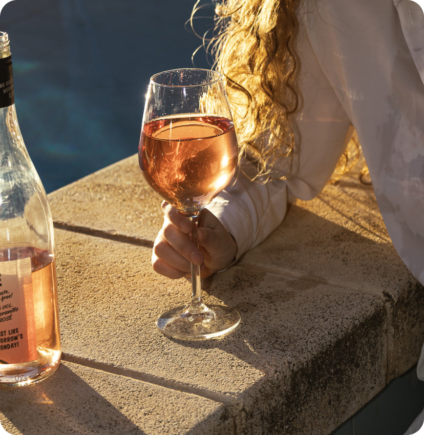 persona sosteniendo una copa de vino Buen Finde al atardecer en la piscina